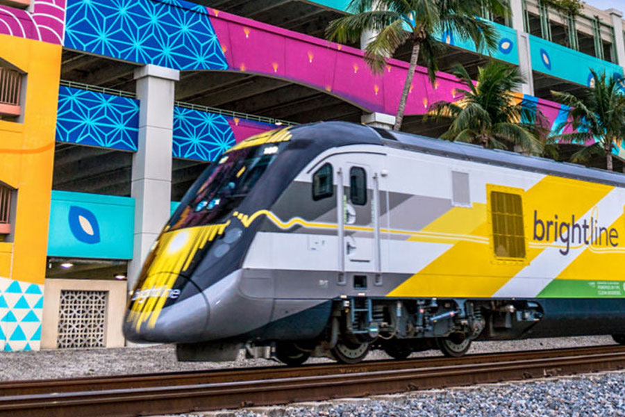Brightline train pulling into a station, with a colorful parking garage in the background.