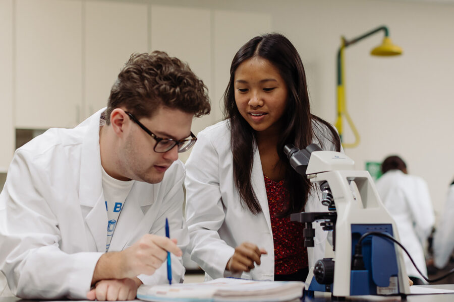 two biology students in a laboratory looking at a specimen in a microscope