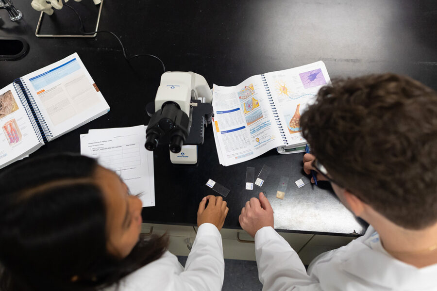 biology students in a laboratory with an open textbook looking into a microscope