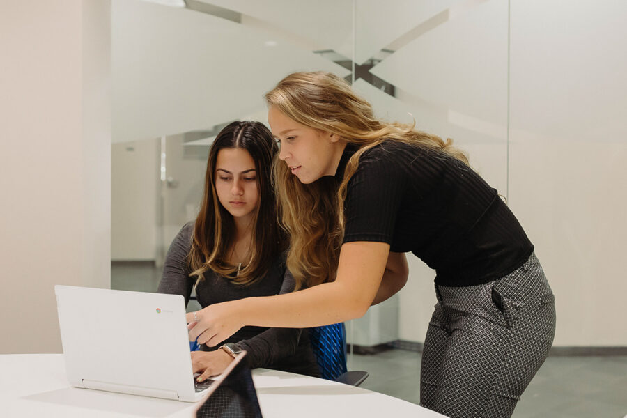 two students look at a computer screen in the library