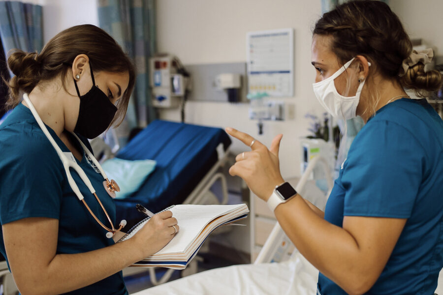 two nursing students talking while one student takes notes in a notebook