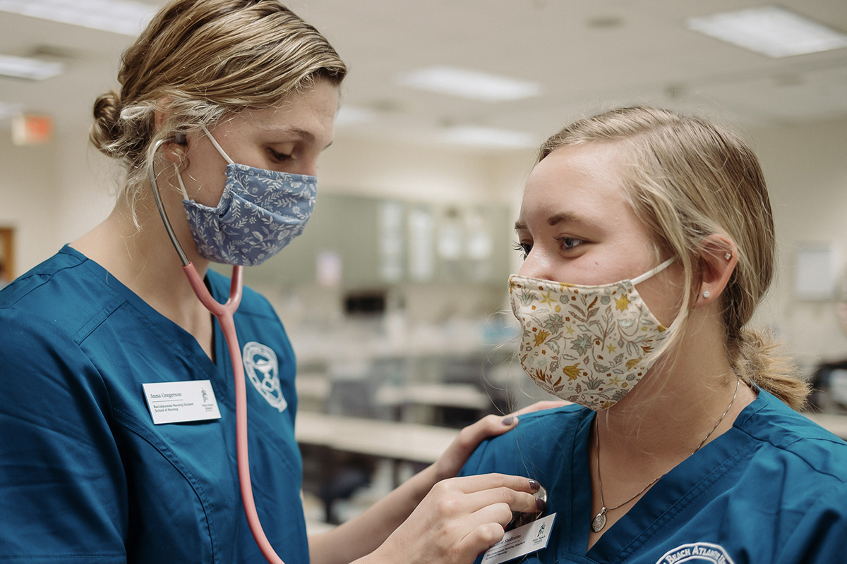a nursing student listening to the heartbeat of another student through a stethoscope