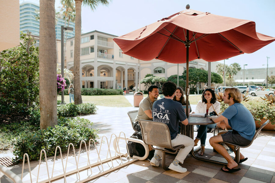 Intercultural studies students sit under an umbrella on campus.