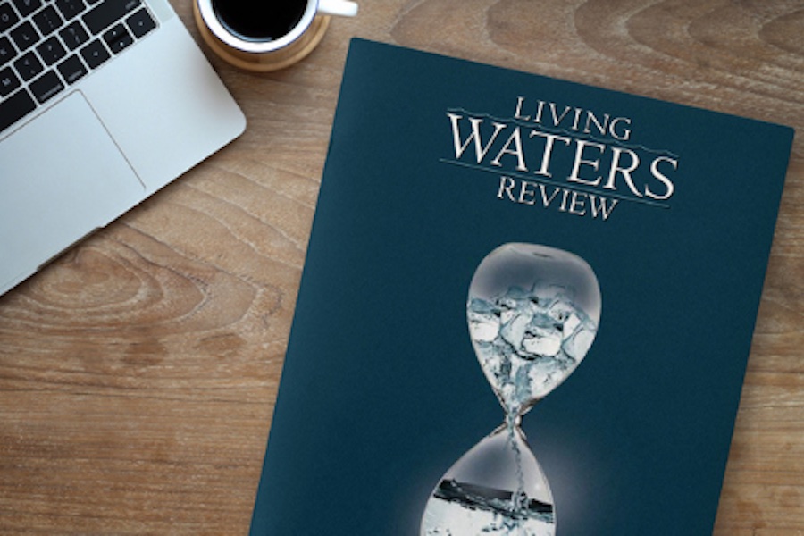 A copy of Living Waters Review sitting on a table next to a laptop computer and a cup of coffee