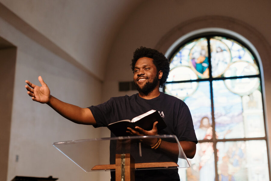 PBA student reads the bible with arm outstretched at the front of chapel.