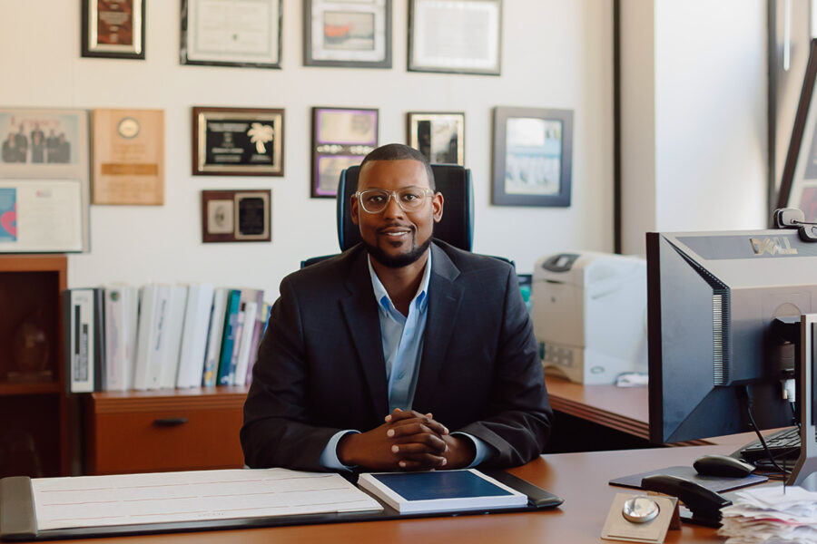 a faculty member sitting behind a desk smiling