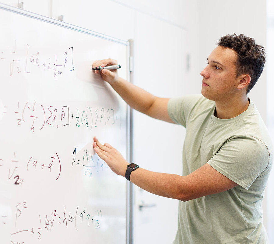 Student from engineering concentration in general engineering program writes equations on a whiteboard.