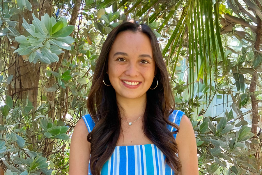 Portrait of Sunshine Tarpey, A student with long dark hair and a blue striped shirt, in front of a leafy background.