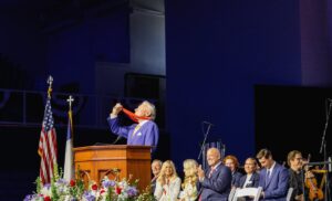 Guests applaud on stage as Thomas Peterffy lifts his golden medal in the air.