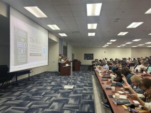 Speaker at podium presents to a crowded room.
